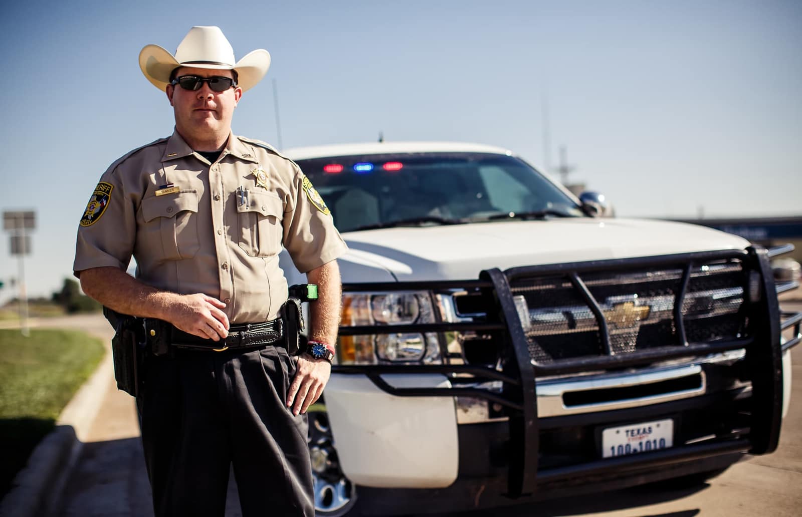 Un agente del sheriff con sombrero blanco junto a su camioneta de patrulla