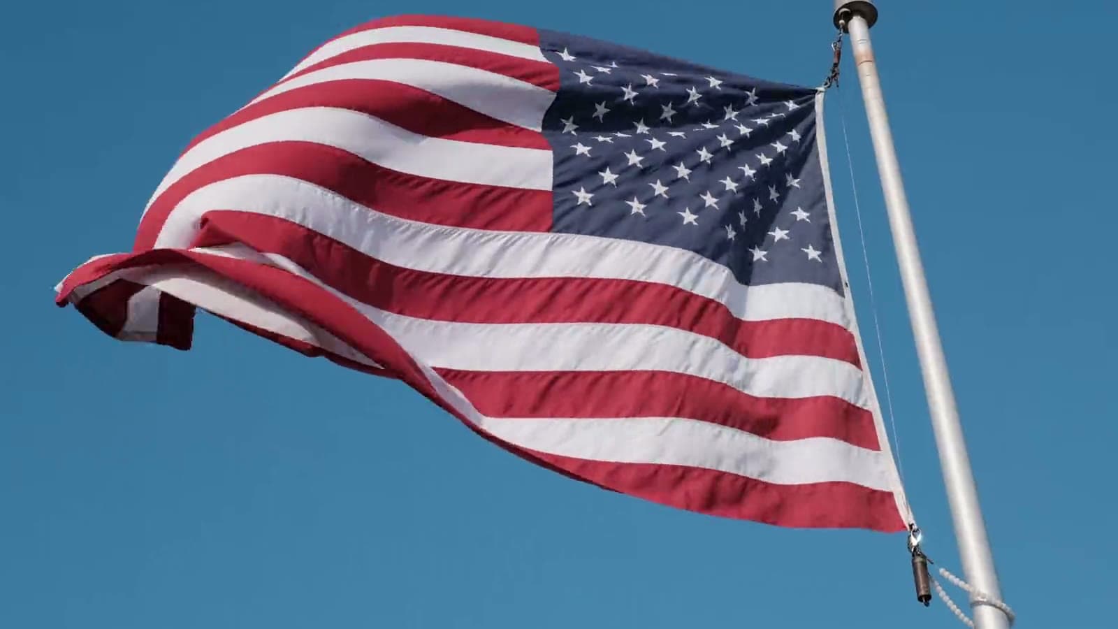 An American flag waving on a flagpole against a blue sky