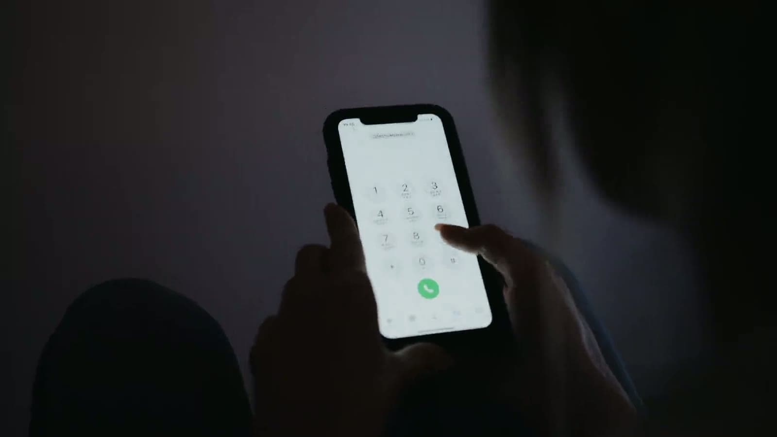 Hands dialing a phone in a dark room