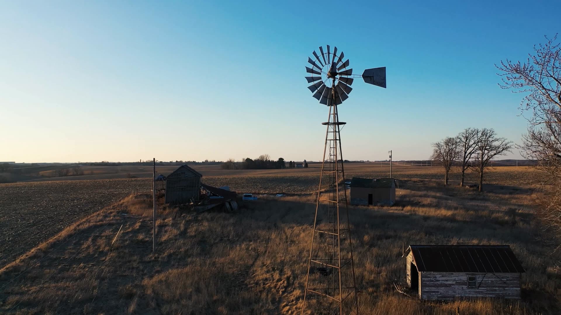 Un viejo molino de viento junto a cobertizos desgastados en un campo seco de invierno al atardecer