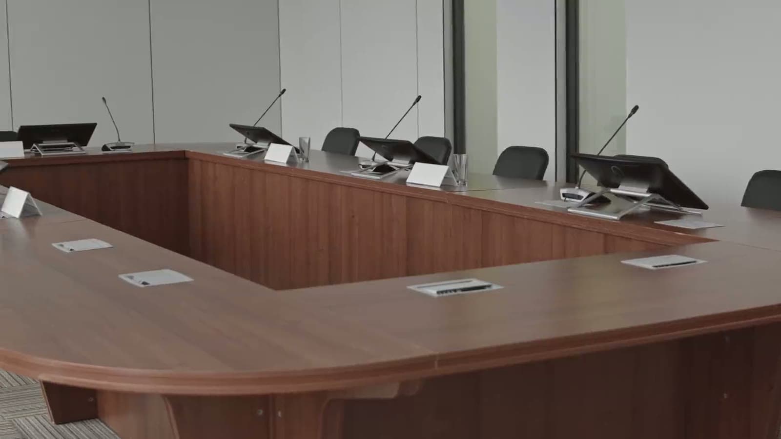 An empty meeting room with a long curved table, microphones, and chairs