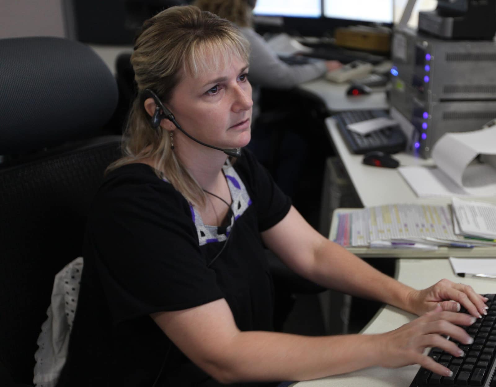 A 911 dispatcher in a headset typing at a console