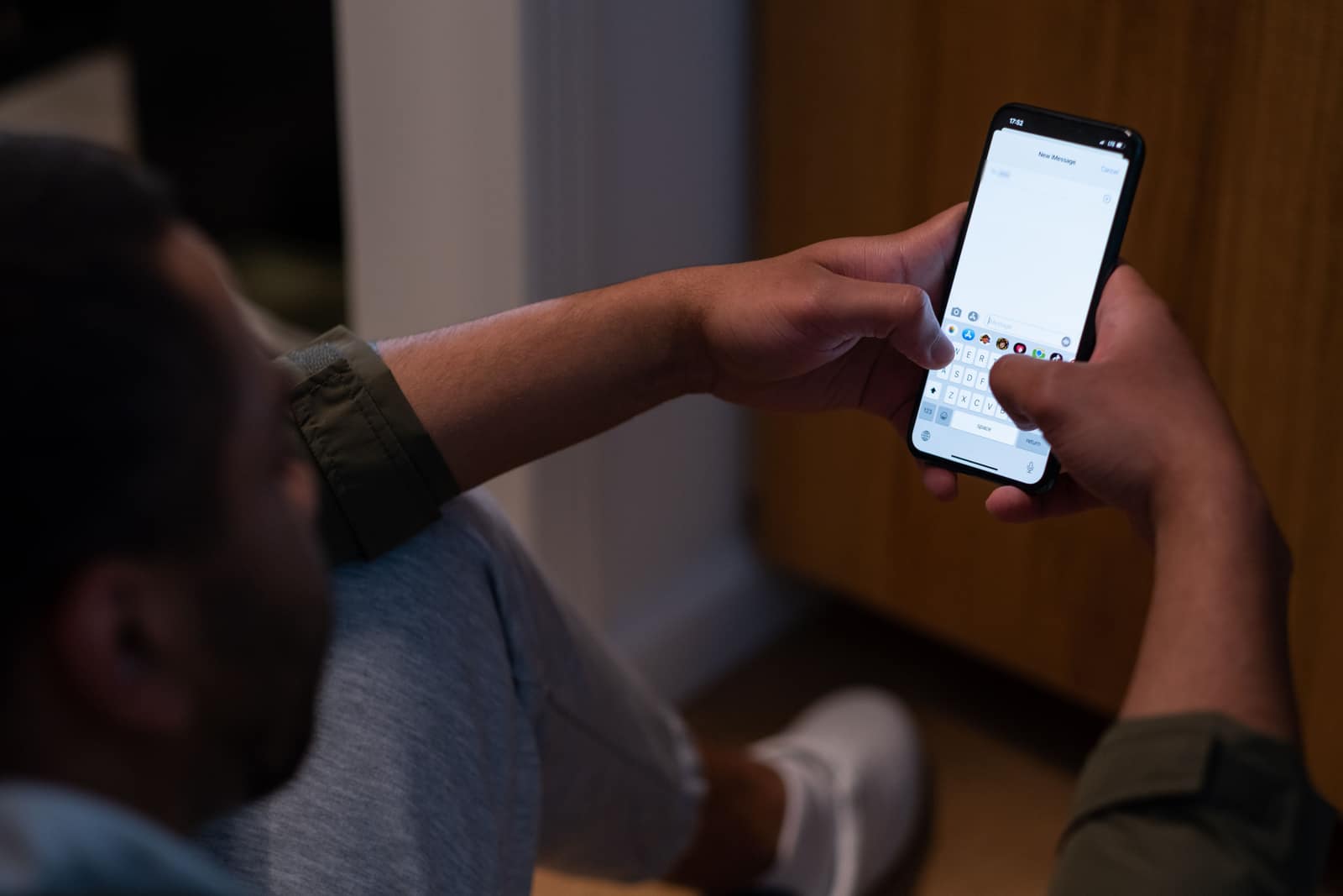 A person in a dim room typing a new text message on a phone